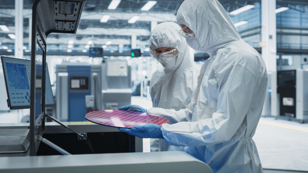 Two people in lab suits holding a semiconductor wafer.